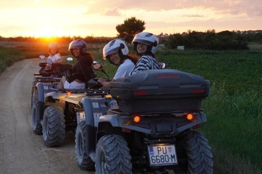 A group of people on ATVs on a dirt road with a sunset in the background. 3
