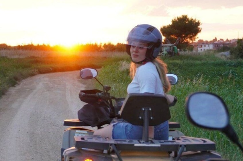 A person on a quad bike on a rural road with a sunset in the background. 2