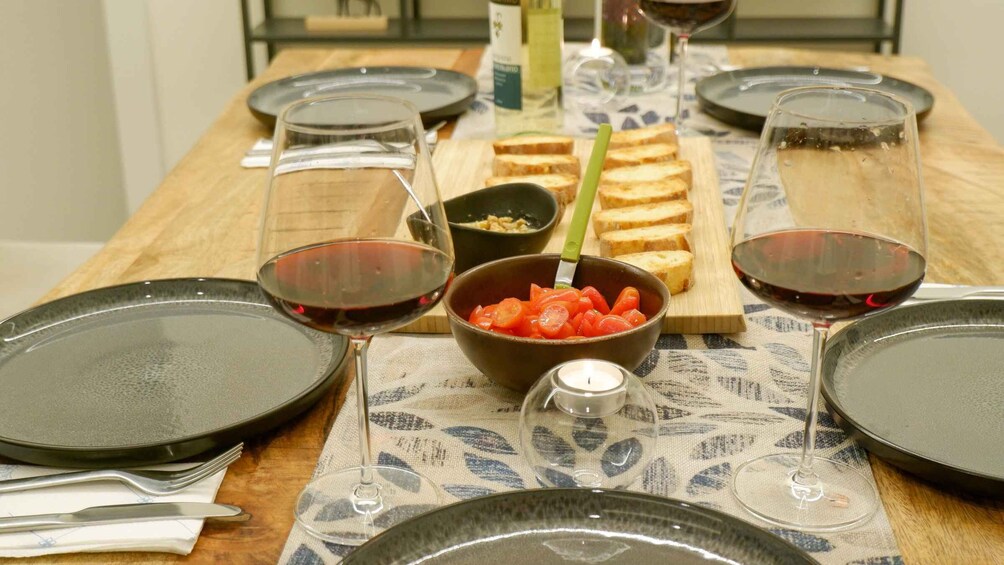 A wooden table with plates, glasses of red wine, a bowl of sliced tomatoes, and a candle. 5