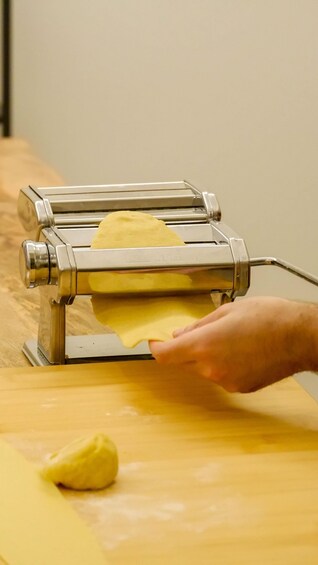 A hand using a pasta machine to roll dough. 4