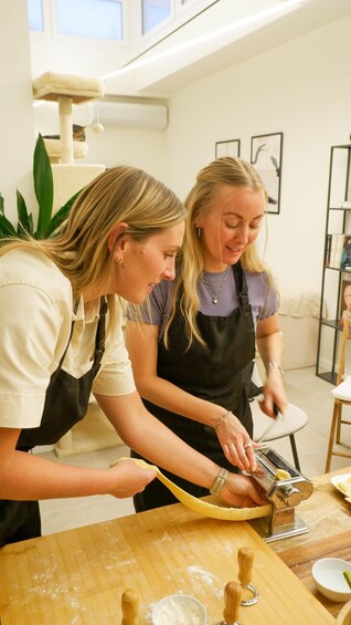 Two people preparing food, one grating cheese, in a kitchen with a cat tree and framed pictures on the wall. 2