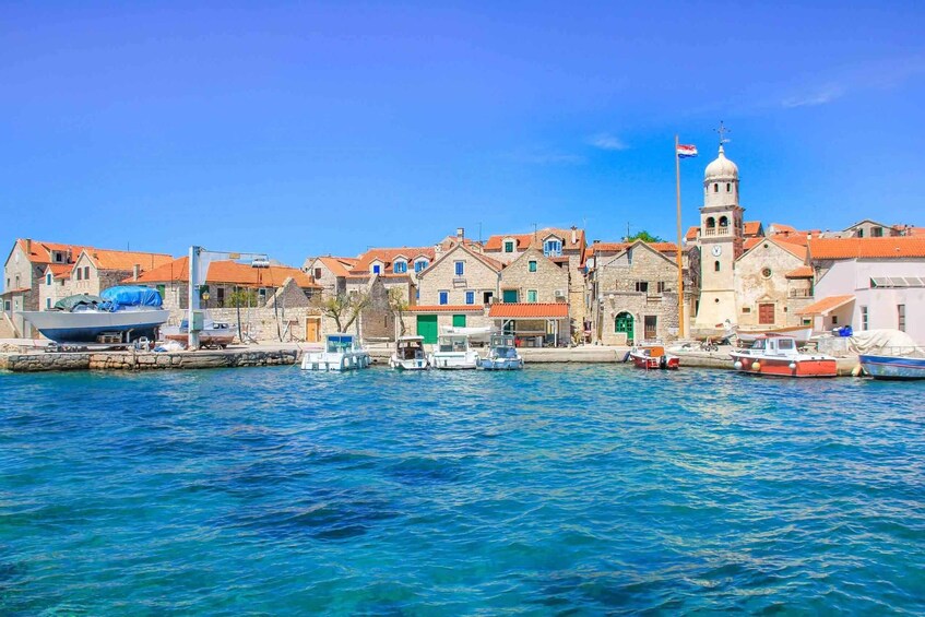 A coastal town with stone buildings, a prominent church with a bell tower, and boats docked along the waterfront. 3