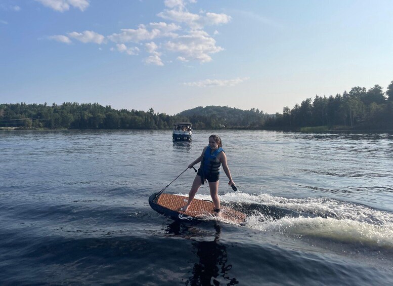 A person wakeboarding on a lake with a boat in the background and a forested shoreline. 5