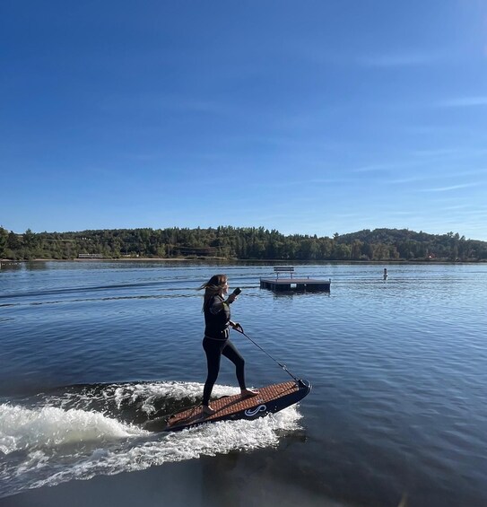A person wakeboarding on a lake with a dock and trees in the background. 1