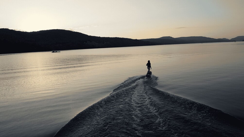 A person wakeboarding on a calm lake with mountains in the background. 4