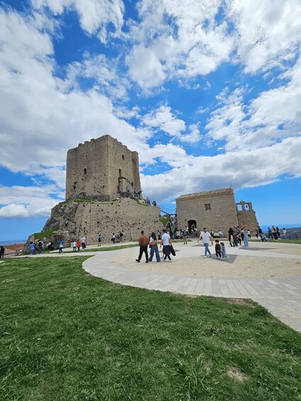 A historic castle on a hill with visitors around. 2