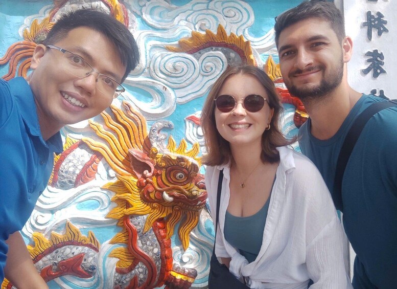 Three people posing in front of a colorful mural with a dragon design. 1
