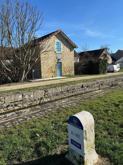 A stone building with a blue door and a sign indicating a distance of 1759 km to Rome. 4