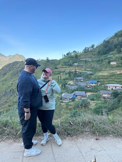Two people standing on a hill overlooking a rural landscape with scattered houses and greenery. 5