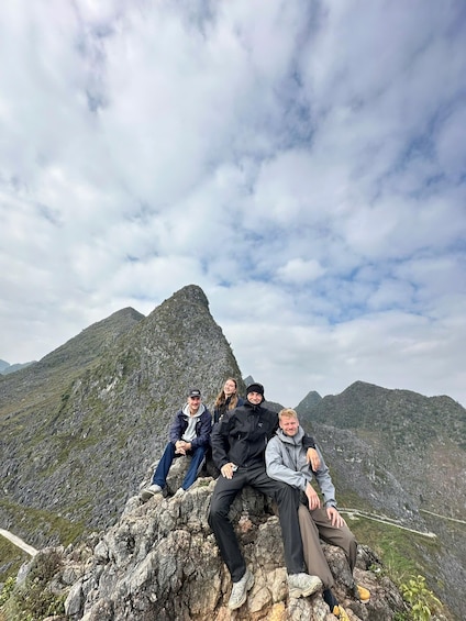 Four people sitting on a rocky outcrop with a mountain in the background. 3