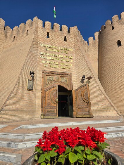 A historical museum entrance with a large, ornate gate and a flag. 1