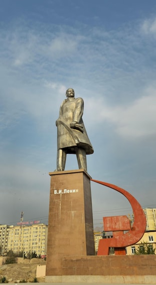 A statue of a man on a pedestal with a curved structure behind it. 3