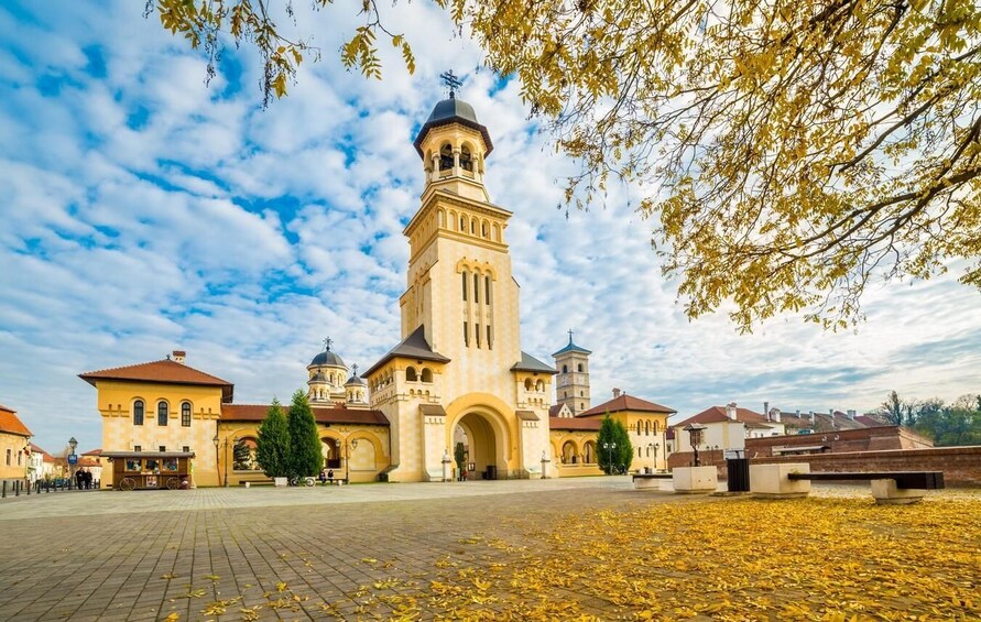 A historic church with a bell tower, surrounded by a paved square and autumn leaves. 1