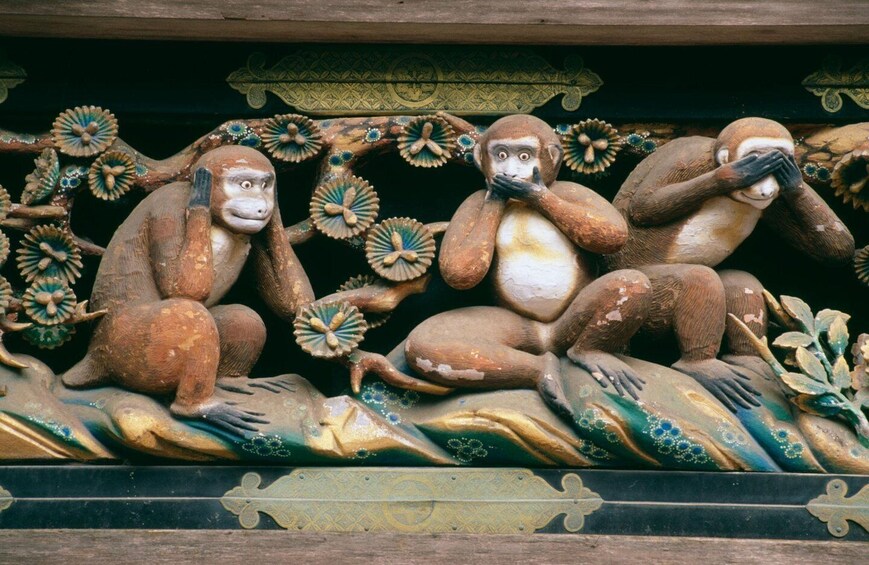 A detailed sculpture of three monkeys with expressive faces, set against a backdrop of ornate floral patterns and a dark, textured surface. 4