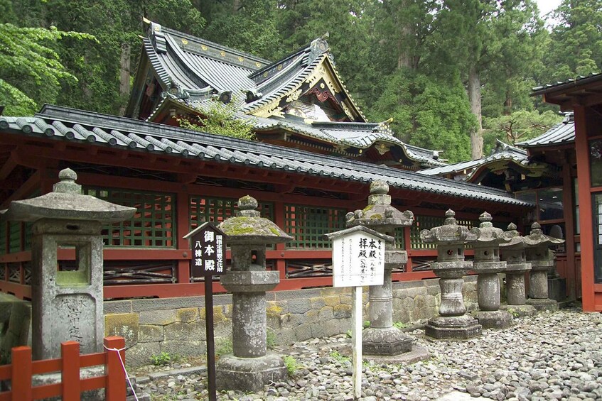 A traditional Japanese temple with ornate architecture, stone lanterns, and a red wooden fence. 2