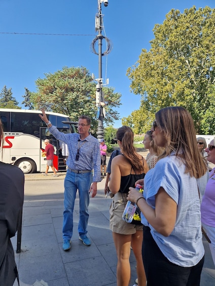 A group of people standing on a sidewalk, a white bus with 'S' on it, and a utility pole with wires. 2