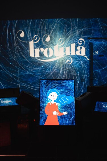 A projection of a character with blue hair and a red dress against a dark background with the word 'Trouva' prominently displayed. 2