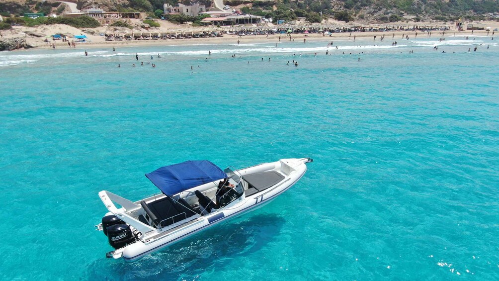 A boat on clear turquoise water with a beach and buildings in the background. 3