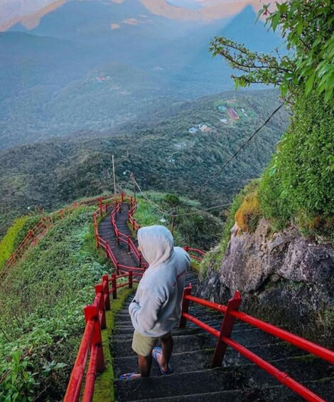A person ascending a red staircase in a mountainous area with lush greenery. 1