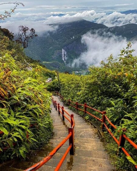 A stone staircase with red railings leading up a mountain, surrounded by lush greenery and a waterfall in the distance. 3