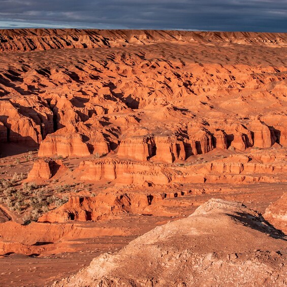 A rugged desert landscape with layered red rock formations and sparse vegetation. 3