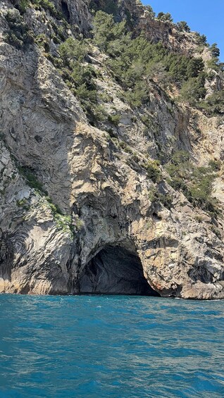 A rocky cliff with a cave entrance and clear blue sea. 2