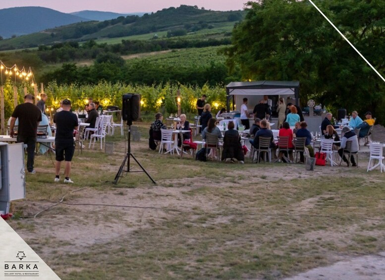An outdoor dining area with tables and chairs, surrounded by greenery and hills. 1