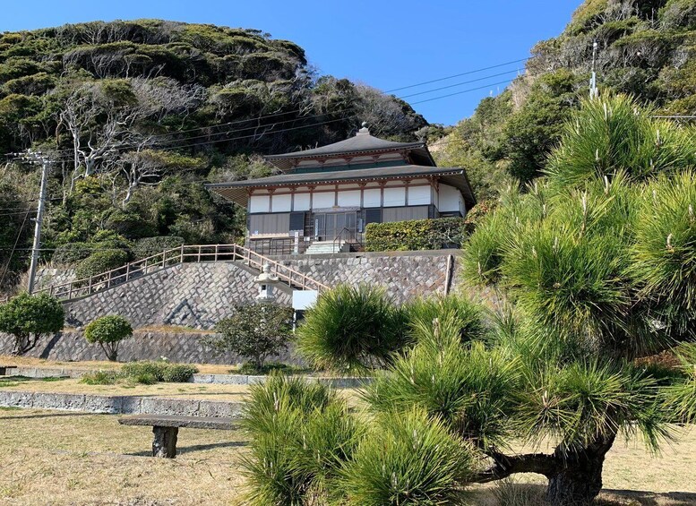 A traditional Japanese building with a stone staircase leading up to it, surrounded by pine trees and a rocky hillside. 3