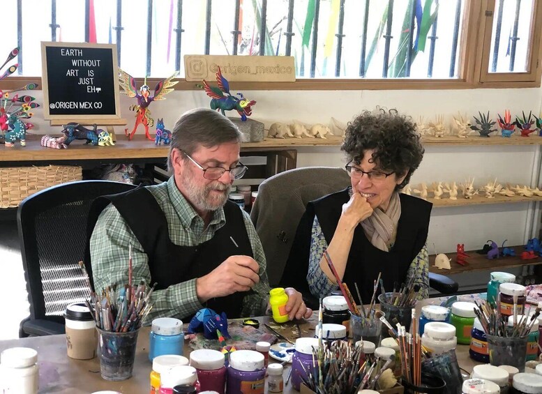 Two people painting in a studio with various art supplies and sculptures on shelves. 3