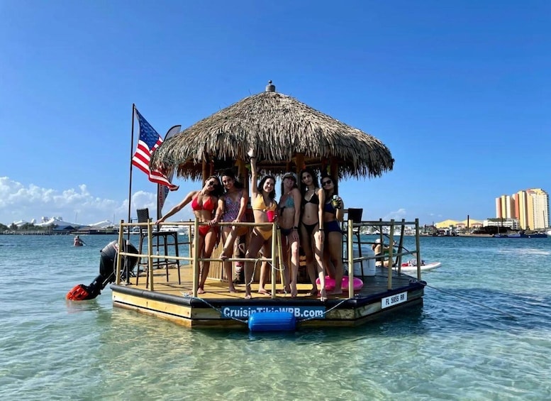A group of people on a floating platform with a thatched roof, surrounded by clear blue water and a city skyline in the background. 5