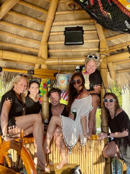 A group of people sitting on a wooden bench under a bamboo structure with a thatched roof. 2