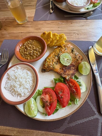 A plate with rice, beans, fried plantains, a grilled fish, and a salad with tomatoes and lime. 3