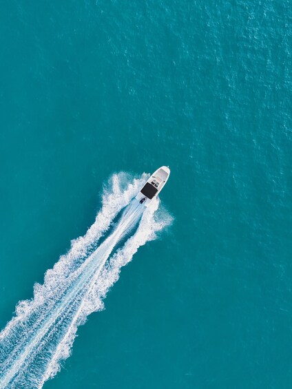 A white boat speeding across turquoise water, creating a wake behind it. 3