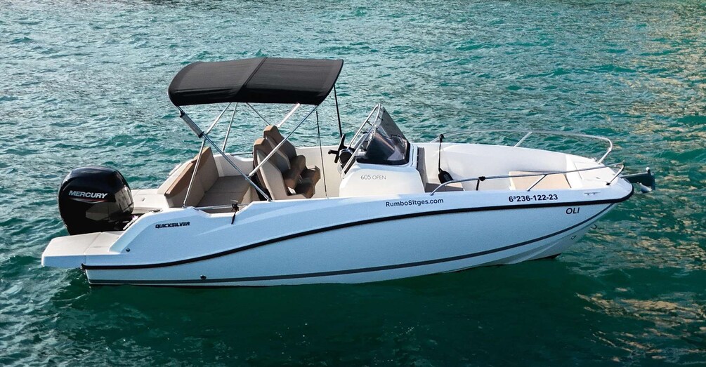 A white motorboat with a black canopy, a Mercury outboard motor, and the name 'RumboSitges.com' on the side. 1