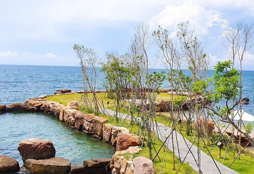 A coastal landscape with a rocky shoreline, a clear blue sea, and a pathway lined with trees. 3