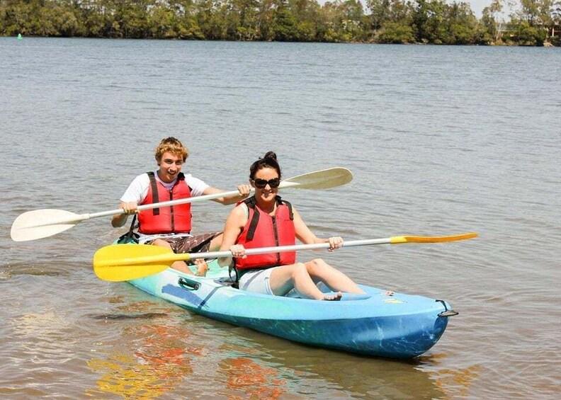 Two people kayaking on a calm lake surrounded by trees. 1