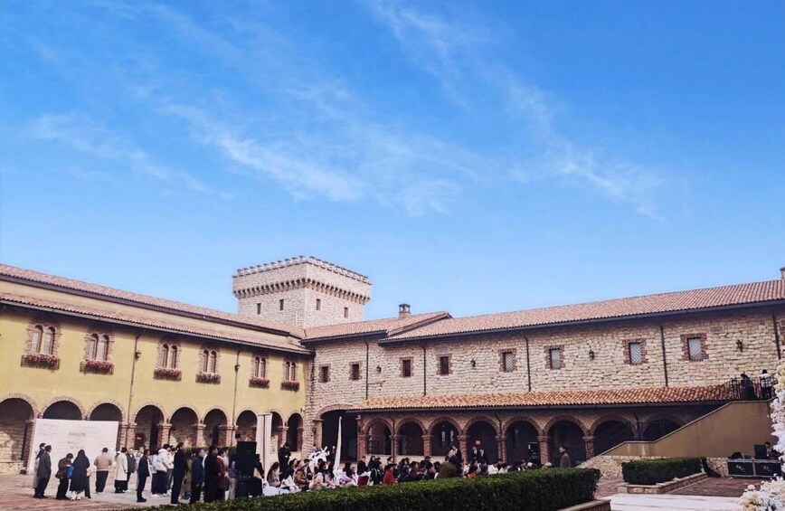 A courtyard with stone buildings, a tower, and people gathered. 4
