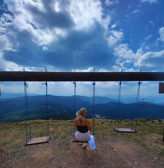 A person sitting on a swing overlooking a mountainous landscape with a clear sky. 2