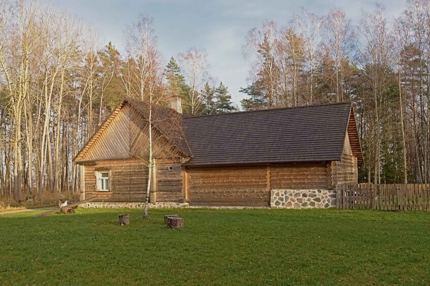 A wooden log cabin with a stone foundation, surrounded by a wooden fence and a grassy yard. 4