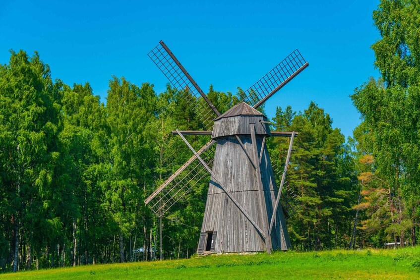 A traditional wooden windmill surrounded by lush green trees and a clear blue sky. 5