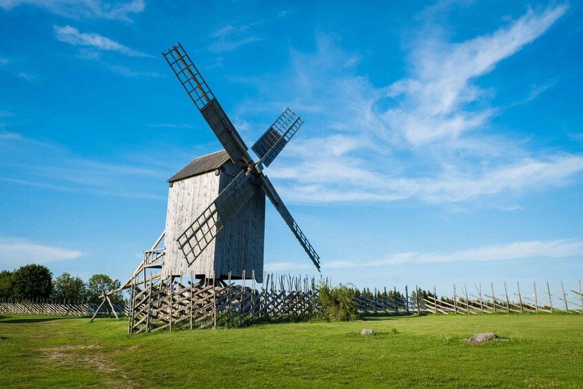 A windmill with a wooden structure and a metal lattice, set in a grassy field with a clear sky. 1