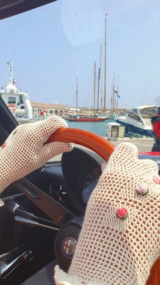 A driver's hands on a steering wheel, a car's dashboard, and a marina with boats in the background. 4