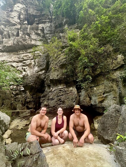 Three people sitting on a rock formation with a cave entrance behind them. 5