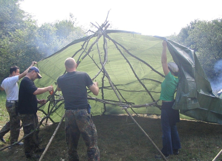 A group of people assembling a large, green, dome-shaped structure with a framework of sticks and branches. 4