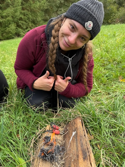 A person sitting on grass near a tree stump with a small fire. 1