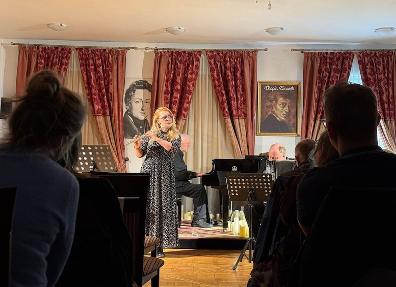 A woman playing a flute on stage with a piano and accordion, in front of a crowd. 5