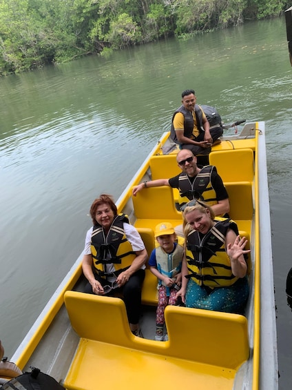 A group of people on a yellow boat with life jackets, surrounded by calm water and greenery. 1