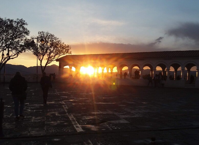 A sunset over a historic building with arches and people walking in the foreground. 5