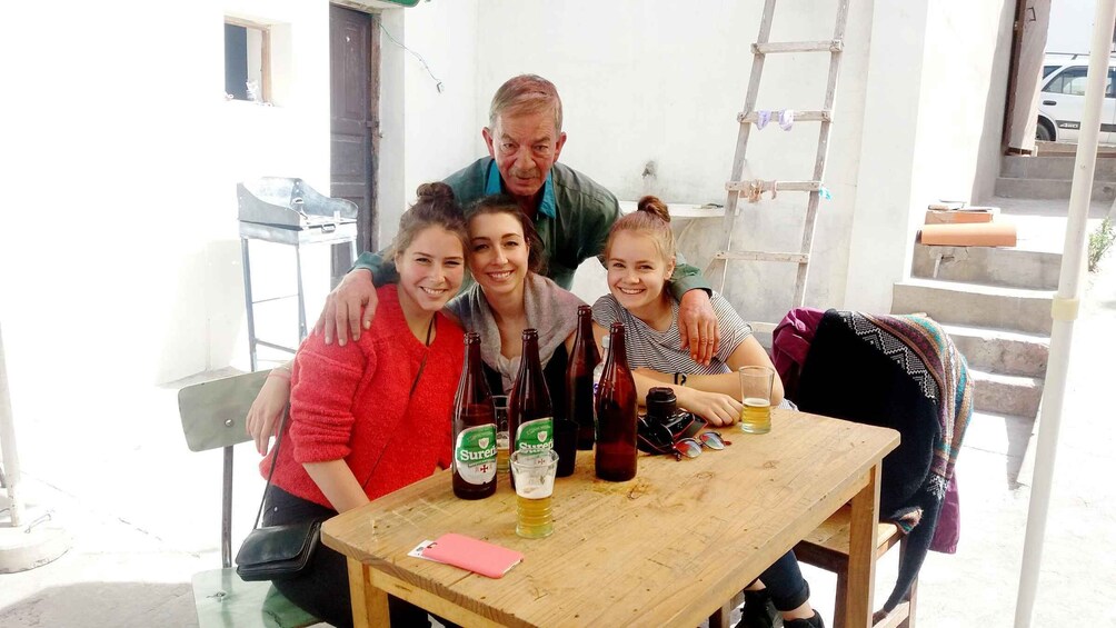 A family of four at a wooden table with bottles and glasses, a ladder, and a white wall in the background. 3