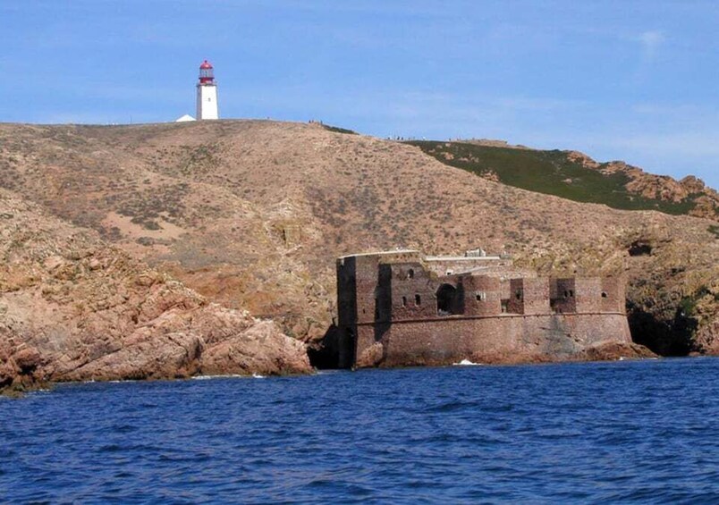 A lighthouse on a hill, a rocky fort, and calm sea. 4